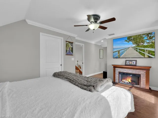 Bedroom featuring crown molding, ceiling fan, a glass covered fireplace, and wood finished floors