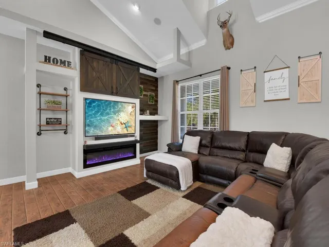 Living room with a barn door, hardwood / wood-style floors, a glass covered fireplace, high vaulted ceiling, and ornamental molding