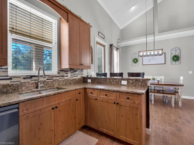 Kitchen featuring light stone counters, stainless steel dishwasher, decorative light fixtures, light wood-style floors, and a peninsula