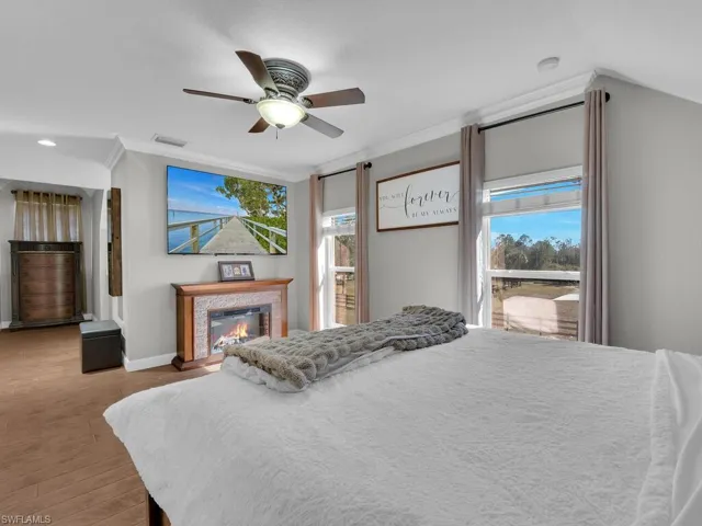 Bedroom featuring crown molding, wood finished floors, a glass covered fireplace, and ceiling fan
