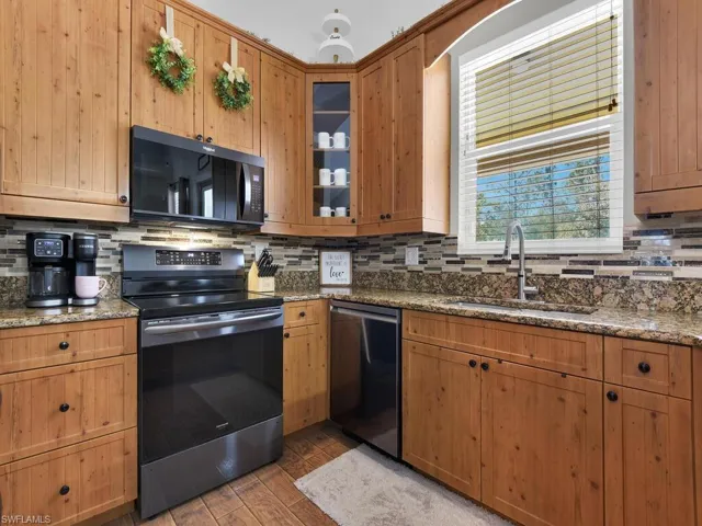 Kitchen with stainless steel appliances, dark stone counters, brown cabinetry, and glass insert cabinets