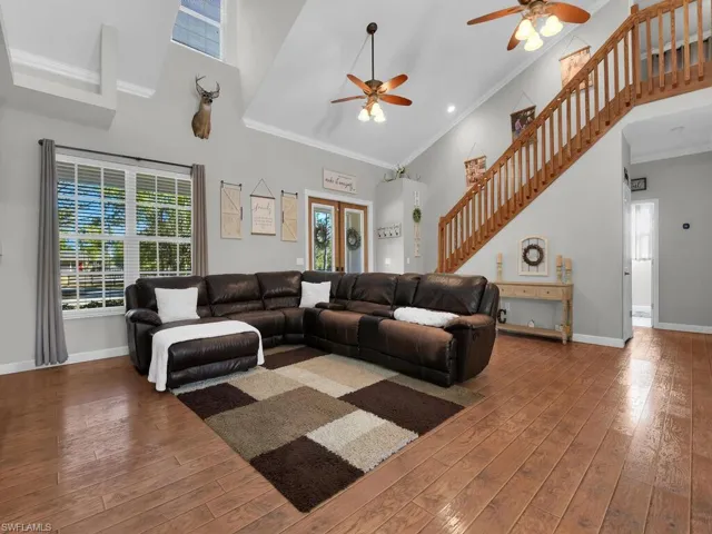 Living room featuring a high ceiling, ceiling fan, hardwood / wood-style flooring, ornamental molding, and stairway