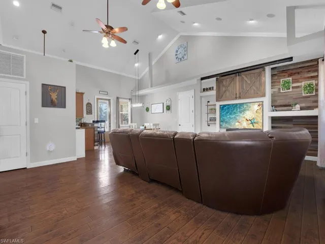 Living area with high vaulted ceiling, dark wood-style floors, ceiling fan, and crown molding