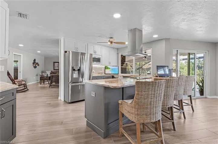 Kitchen featuring light stone countertops, a kitchen breakfast bar, stainless steel appliances, and island range hood.