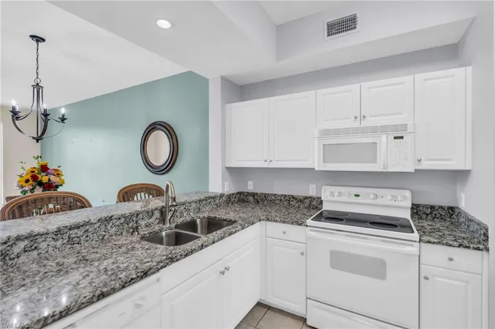 Kitchen with light tile patterned floors, white appliances, a chandelier, white cabinetry, and sink