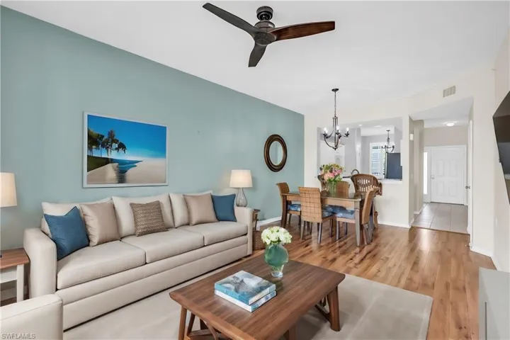 Living room with light wood-type flooring and ceiling fan with notable chandelier