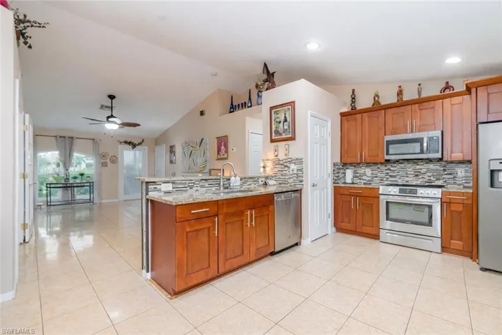 Kitchen featuring stainless steel appliances, wood finish cabinetry, a peninsula, decorative backsplash, and light stone countertops