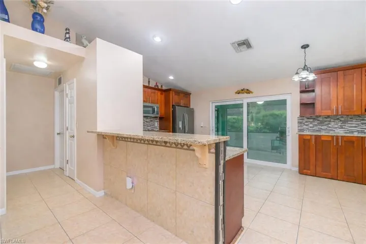 Kitchen featuring vaulted ceiling, wood finish cabinetry, a breakfast bar area, a peninsula, and backsplash