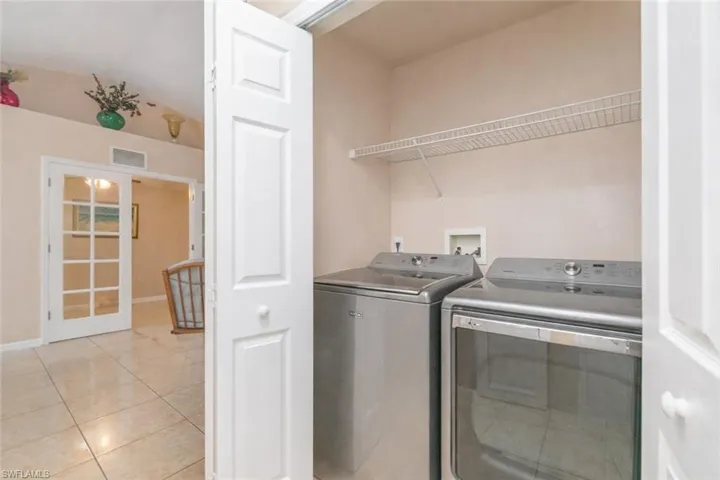 Laundry area with washing machine and clothes dryer, light tile patterned flooring, and lofted ceiling