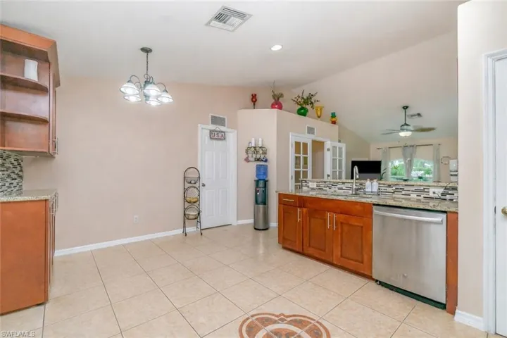 Kitchen with backsplash, light stone counters, dishwasher, wood finish cabinets, and lofted ceiling