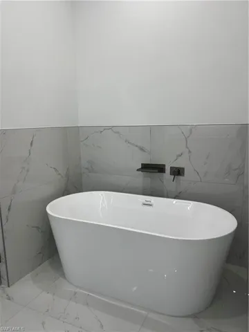 Full bath with wainscoting, marble tiled floors, a freestanding bath, and tile walls