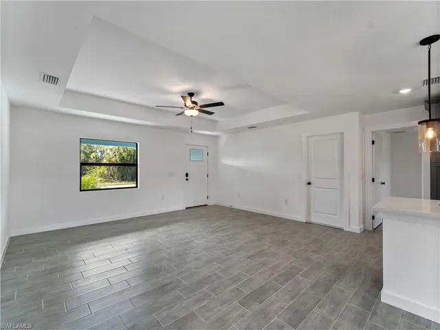 Unfurnished living room with a raised ceiling, ceiling fan, and wood finish floors