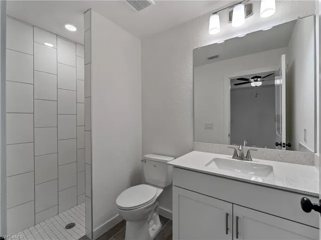 Full bath featuring a textured wall, vanity, ceiling fan, and tiled shower