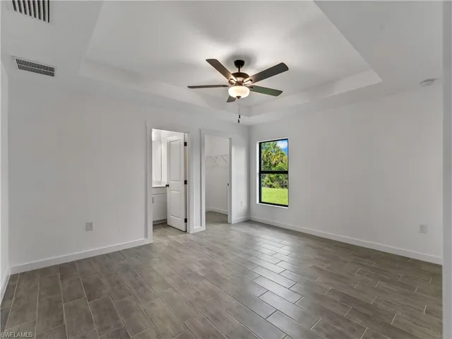 Unfurnished bedroom featuring a raised ceiling, wood finish floors, a walk in closet, and a ceiling fan