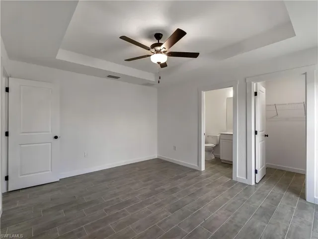 Unfurnished bedroom with a raised ceiling, a walk in closet, dark wood-style flooring, and a ceiling fan