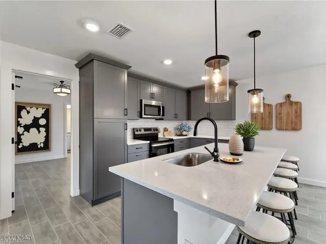 Virtually Staged  Kitchen with gray cabinets, a breakfast bar area, light stone countertops, backsplash, and recessed lighting