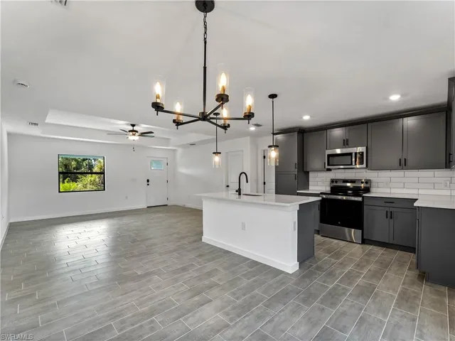 Kitchen with appliances with stainless steel finishes, backsplash, hanging light fixtures, ceiling fan, and a center island with sink