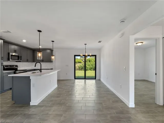 Kitchen with gray cabinets, decorative light fixtures, backsplash, appliances with stainless steel finishes, and wood tiled floors