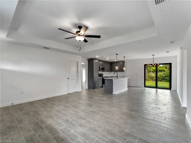 Unfurnished living room featuring a raised ceiling, ceiling fan, and wood finish floors