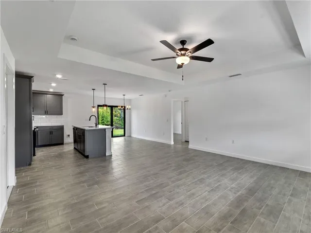 Unfurnished living room featuring a tray ceiling, light wood-style flooring, a chandelier, and ceiling fan