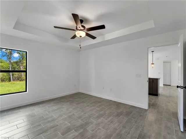 Empty room with a raised ceiling, wood tiled floors, and a ceiling fan