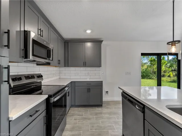 Kitchen featuring appliances with stainless steel finishes, gray cabinets, light stone counters, backsplash, and a textured ceiling