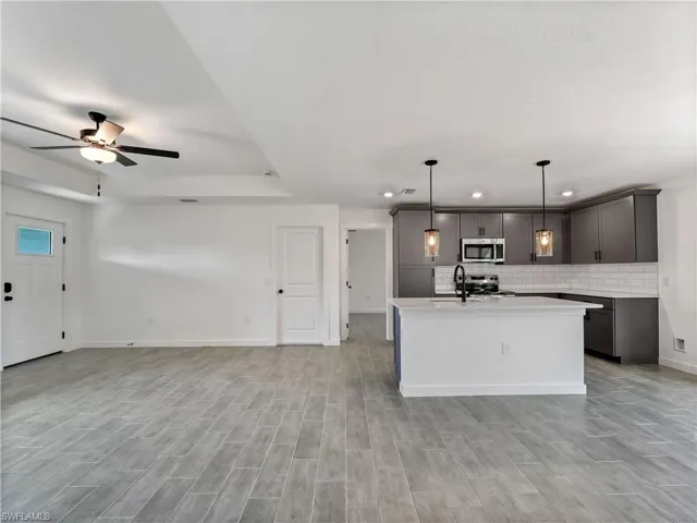 Kitchen with open floor plan, gray cabinets, tasteful backsplash, a kitchen island with sink, and decorative light fixtures