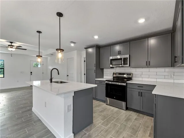 Kitchen with stainless steel appliances, light stone countertops, gray cabinets, pendant lighting, and recessed lighting