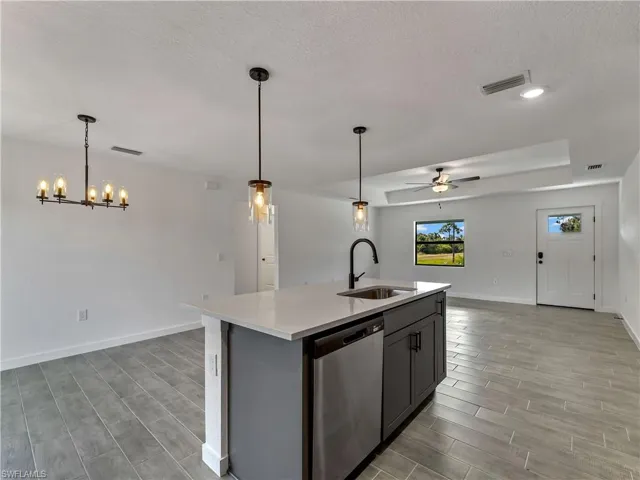 Kitchen featuring open floor plan, a center island with sink, stainless steel dishwasher, wood finish floors, and decorative light fixtures