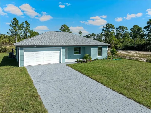 Ranch-style house with a shingled roof, decorative driveway, a front lawn, and an attached garage