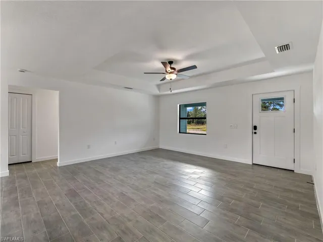Unfurnished living room featuring a tray ceiling, light wood-style flooring, a chandelier, and ceiling fan