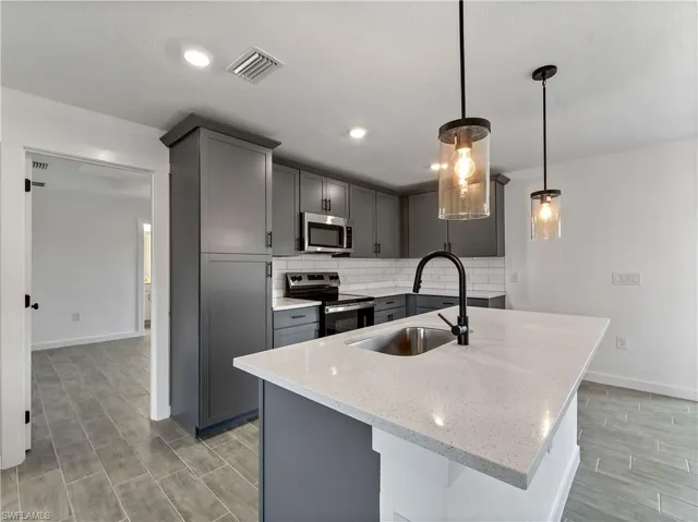 Kitchen featuring appliances with stainless steel finishes, gray cabinets, light stone countertops, decorative backsplash, and wood tiled floors