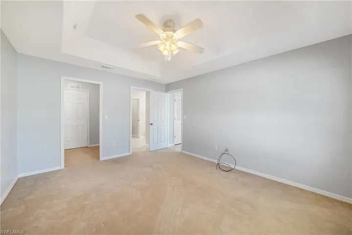Unfurnished bedroom with a tray ceiling, ceiling fan, and light carpet