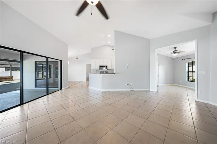 Unfurnished living room featuring light tile patterned floors, ceiling fan, and lofted ceiling