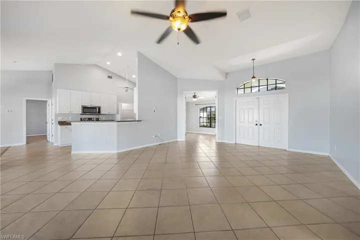 Unfurnished living room with light tile patterned floors, high vaulted ceiling, and ceiling fan