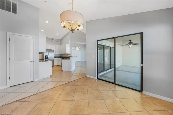 Tiled empty room featuring ceiling fan with notable chandelier and high vaulted ceiling