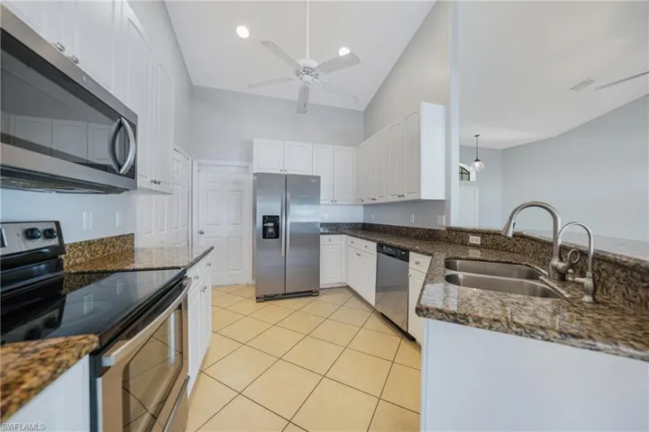Kitchen with white cabinetry, sink, appliances with stainless steel finishes, and dark stone counters
