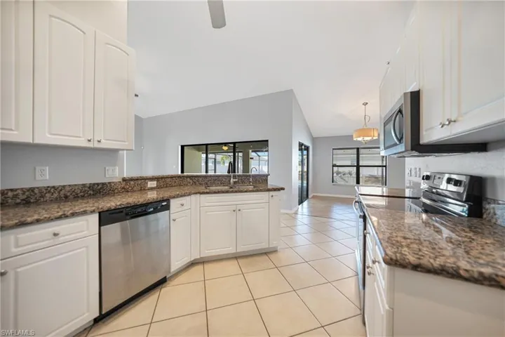 Kitchen with a healthy amount of sunlight, white cabinetry, stainless steel appliances, and vaulted ceiling
