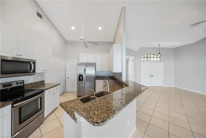 Kitchen featuring high vaulted ceiling, stainless steel appliances, white cabinetry, and ceiling fan