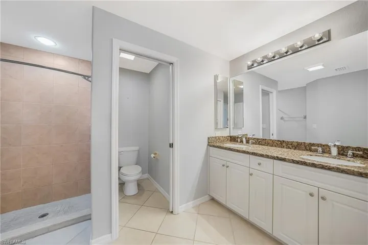 Bathroom with tiled shower, tile patterned flooring, vanity, and toilet