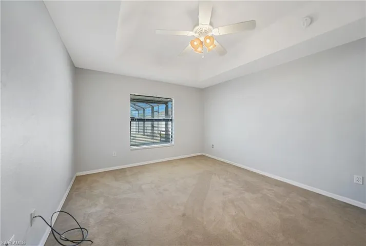 Spare room featuring a tray ceiling, light carpet, and ceiling fan