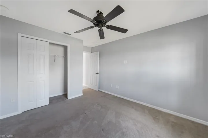 Unfurnished bedroom with ceiling fan, dark carpet, and a closet