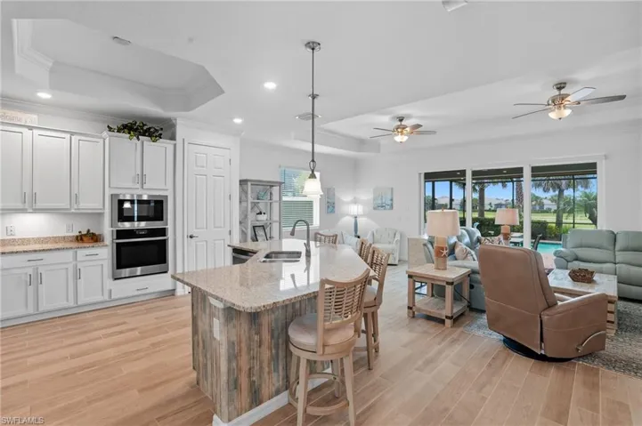 Kitchen featuring a raised ceiling, hanging light fixtures, crown molding, light stone countertops, and open floor plan