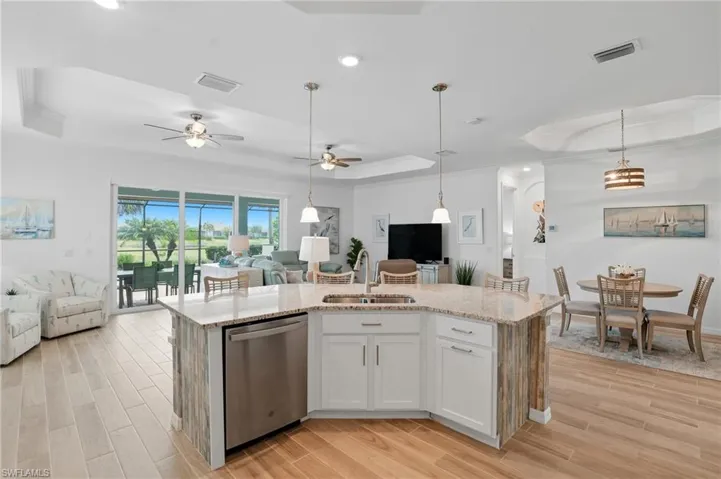 Kitchen with a raised ceiling, open floor plan, light stone counters, dishwasher, and light wood-style floors