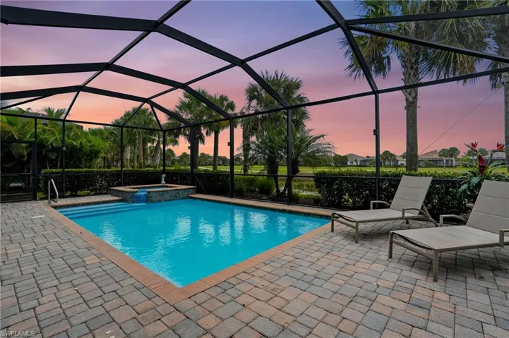 Pool at dusk featuring glass enclosure, a pool with connected hot tub, a sunroom, and a patio area