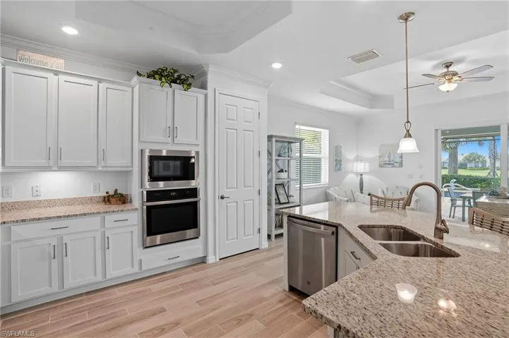 Kitchen featuring a raised ceiling, ornamental molding, stainless steel appliances, decorative light fixtures, and light stone countertops