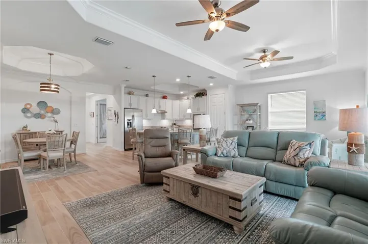 Living area featuring a raised ceiling, crown molding, light wood finished floors, and a ceiling fan