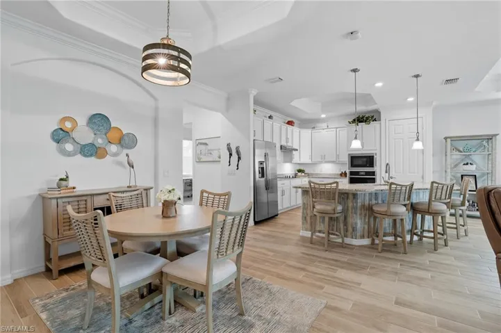 Dining room with a raised ceiling, crown molding, light wood-style flooring, and recessed lighting