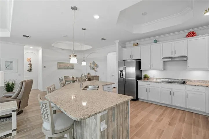 Kitchen with crown molding, a breakfast bar area, a tray ceiling, decorative light fixtures, and stainless steel fridge
