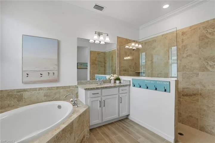 Bathroom featuring a garden tub, vanity, crown molding, a walk in shower, and wood finish floors